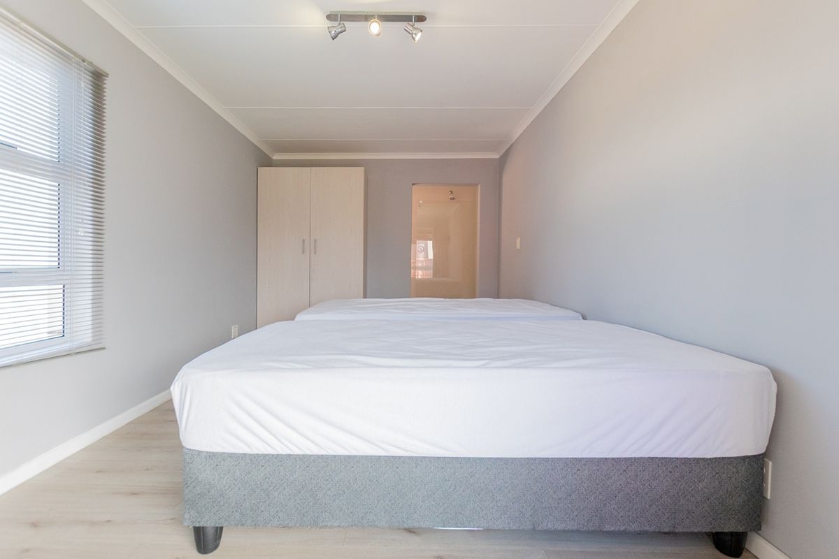 A clean, neutral bedroom featuring light laminate flooring, a built-in wardrobe, and a window with venetian blinds.