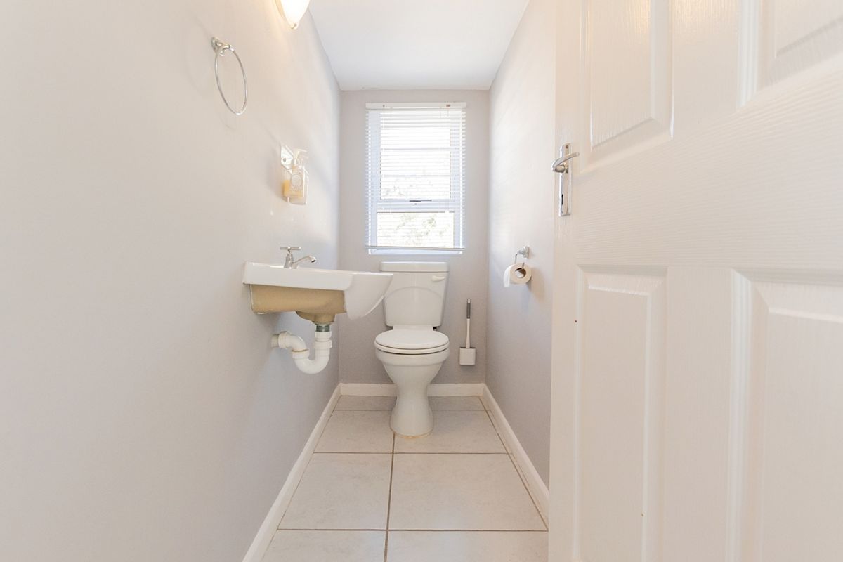 A clean and functional guest bathroom featuring a wall-mounted basin, toilet, and neutral tiled flooring with natural light from a window.
