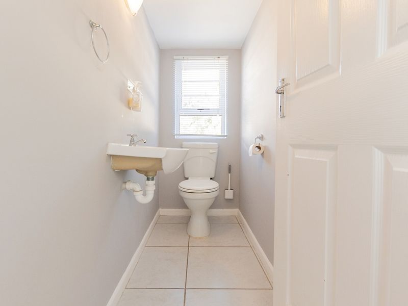 A clean and functional guest bathroom featuring a wall-mounted basin, toilet, and neutral tiled flooring with natural light from a window.