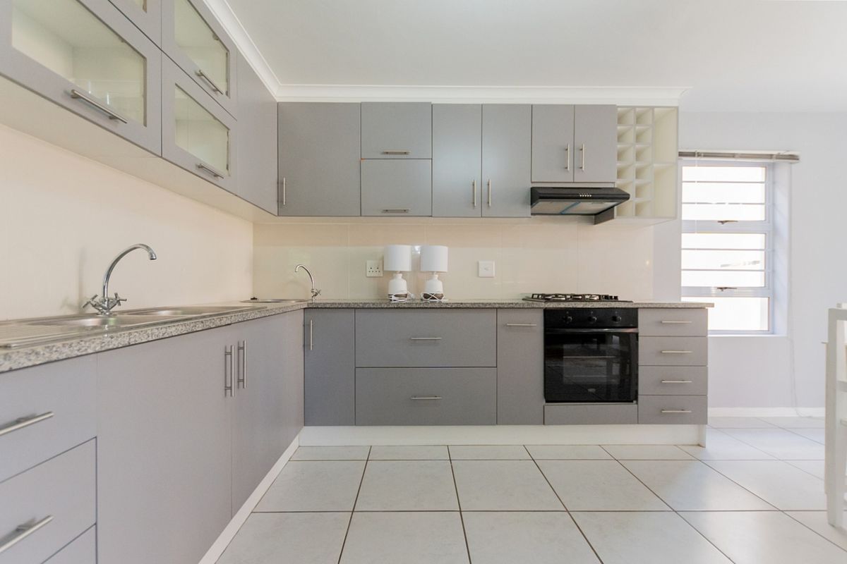 Modern kitchen featuring grey cabinetry, granite countertops, built-in oven, gas hob, extractor fan, and tiled flooring.