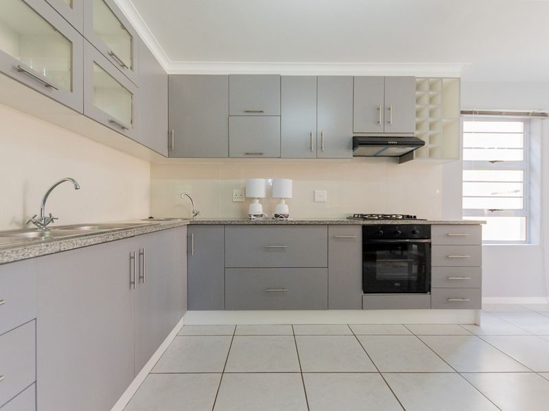 Modern kitchen featuring grey cabinetry, granite countertops, built-in oven, gas hob, extractor fan, and tiled flooring.