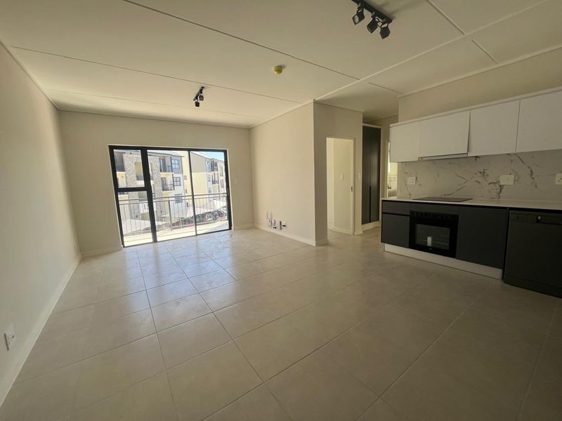 Modern open-plan living area featuring tiled floors, a sleek kitchen with built-in appliances, and a sliding door leading to a balcony.
