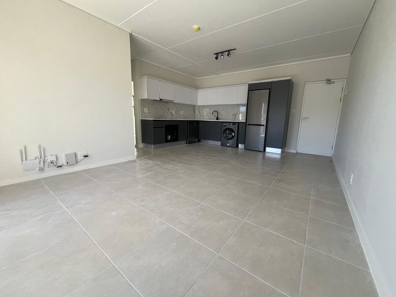 Modern open-plan living area featuring a sleek kitchen with two-tone cabinetry, marble-look splashback, and neutral tiled flooring throughout.