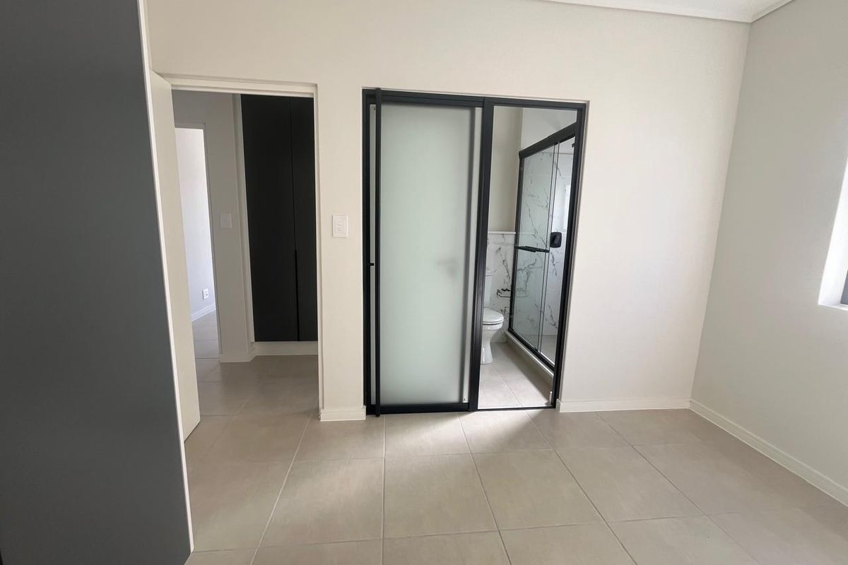 Modern bedroom featuring neutral tiled flooring, built-in storage, and a sleek en-suite bathroom with a contemporary glass-enclosed shower.