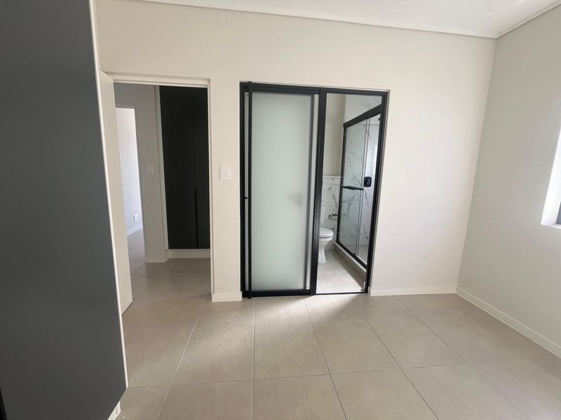 Modern bedroom featuring neutral tiled flooring, built-in storage, and a sleek en-suite bathroom with a contemporary glass-enclosed shower.