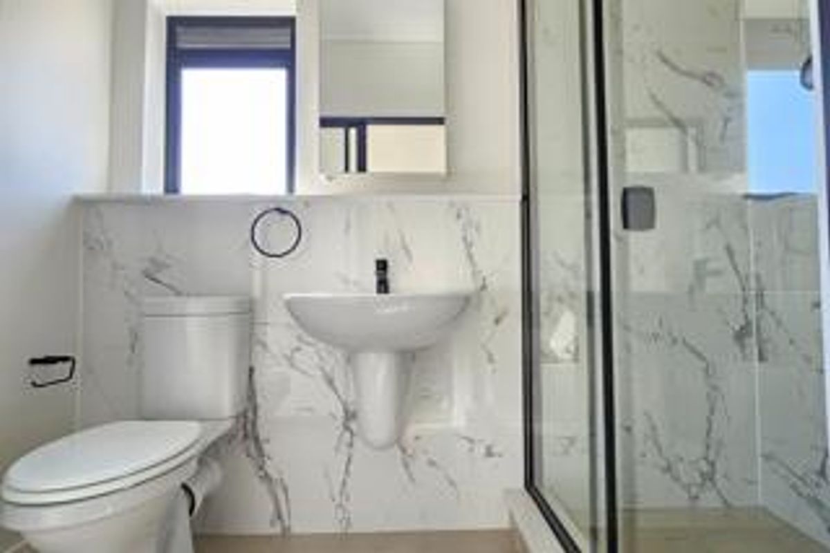 Modern bathroom featuring a pedestal washbasin, toilet, and a glass-enclosed shower with elegant marble-look wall tiling.