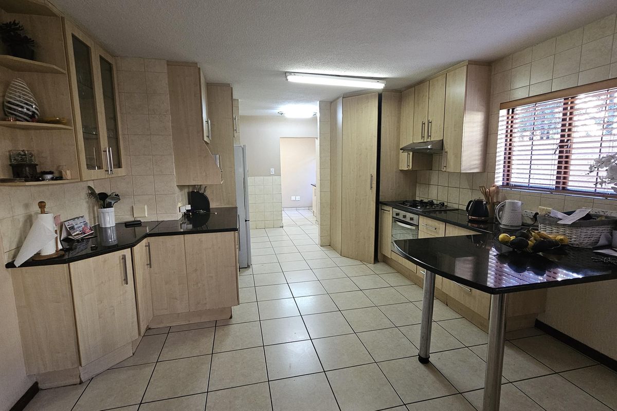 A functional kitchen featuring light wood cabinetry, black granite countertops, a gas hob, built-in oven, and a breakfast bar with tiled flooring throughout.