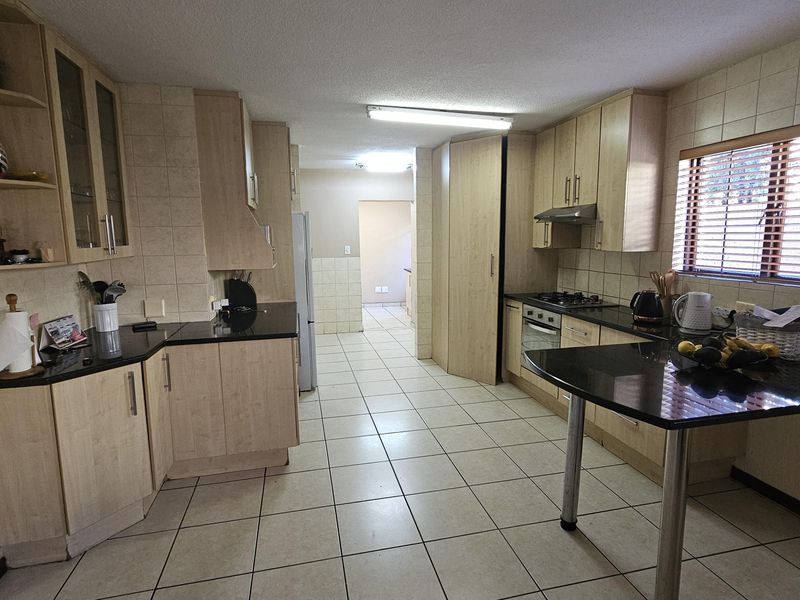 A functional kitchen featuring light wood cabinetry, black granite countertops, a gas hob, built-in oven, and a breakfast bar with tiled flooring throughout.