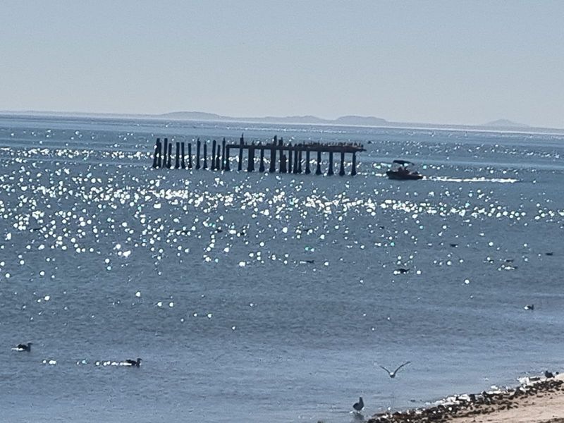 A scenic view of the ocean featuring a distant pier structure and a small boat on the water.
