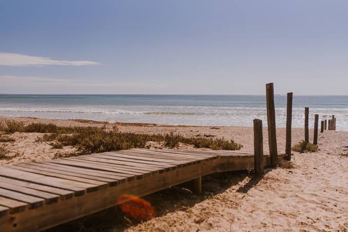 A scenic view of the ocean featuring a wooden boardwalk leading towards the beach with timber post markers.