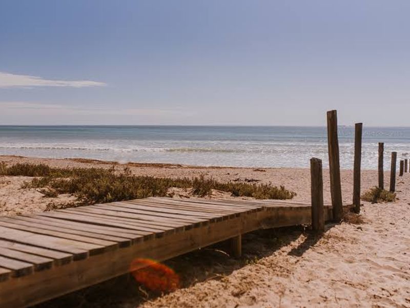 A scenic view of the ocean featuring a wooden boardwalk leading towards the beach with timber post markers.