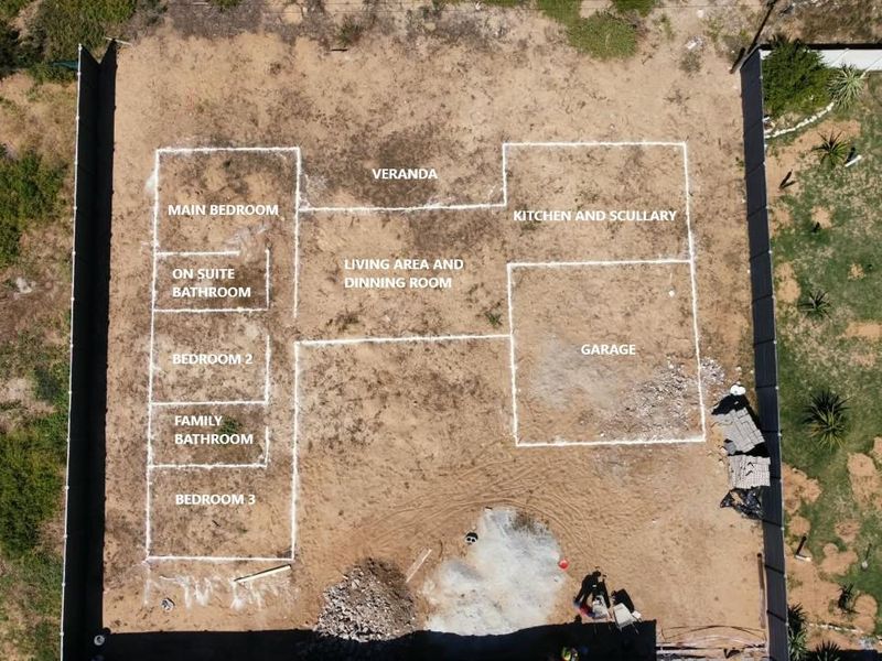 Aerial view of a property plot with white markings indicating the proposed layout for a house, including bedrooms, living areas, and garage.
