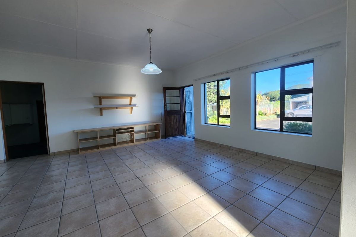 A bright, open-plan living area featuring neutral tiled flooring, large windows providing natural light, and built-in shelving units.