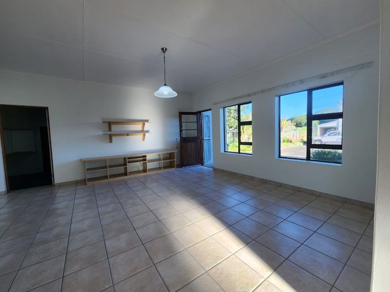 A bright, open-plan living area featuring neutral tiled flooring, large windows providing natural light, and built-in shelving units.