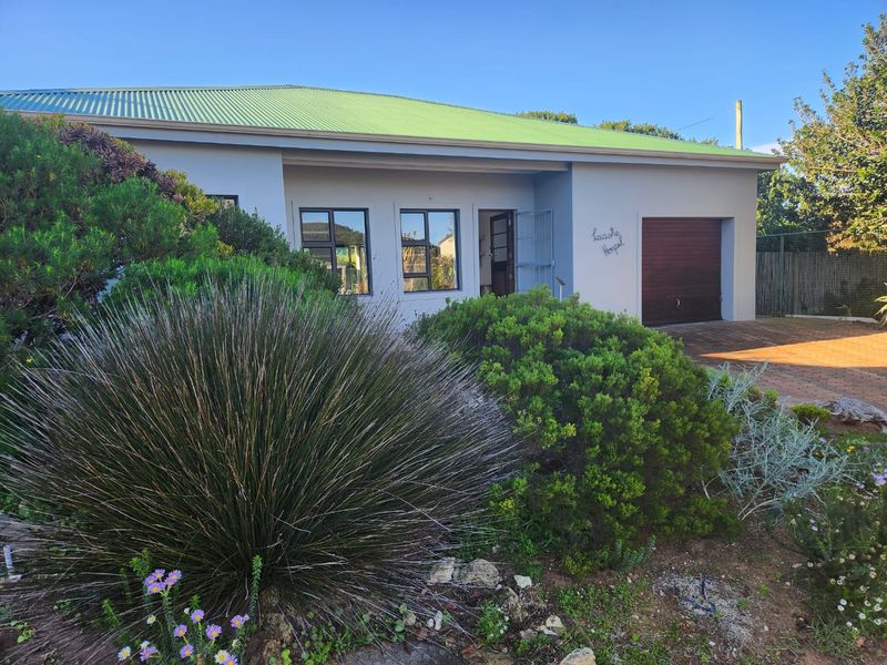 Front elevation of a single-story house featuring a green metal roof, paved driveway, and an integrated garage.