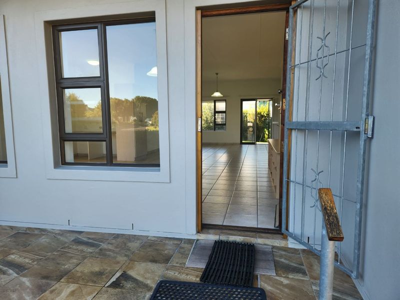Entrance view showing a security gate, tiled patio area, and a clear line of sight into the open plan living space.