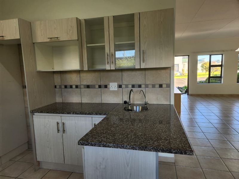 A clean, functional kitchen area featuring granite countertops, light wood-finish cabinetry, and a tiled backsplash, flowing into an open-plan living space.