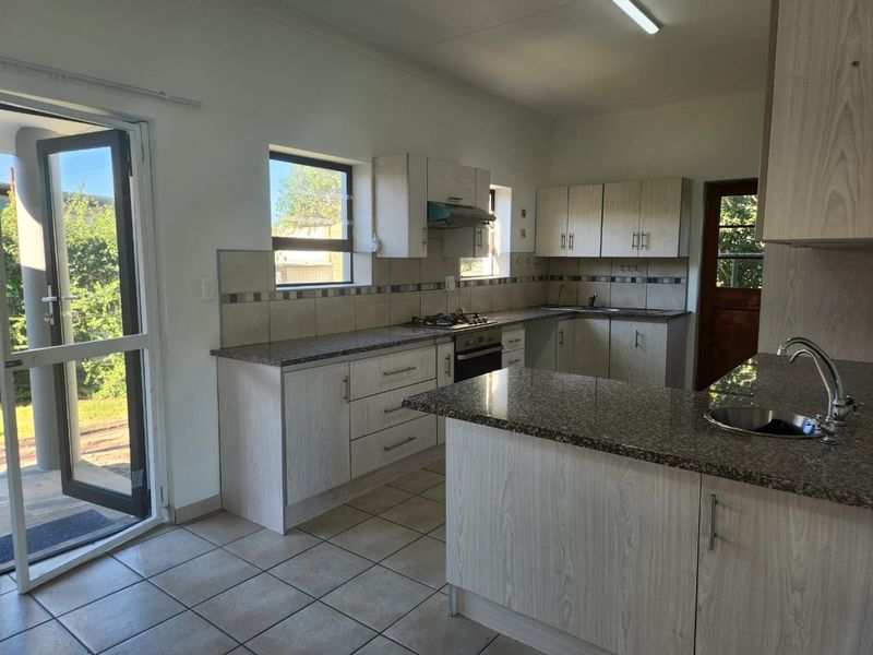 A functional kitchen featuring light wood-grain cabinetry, granite countertops, a gas hob, and tiled flooring with direct access to the outdoor area.