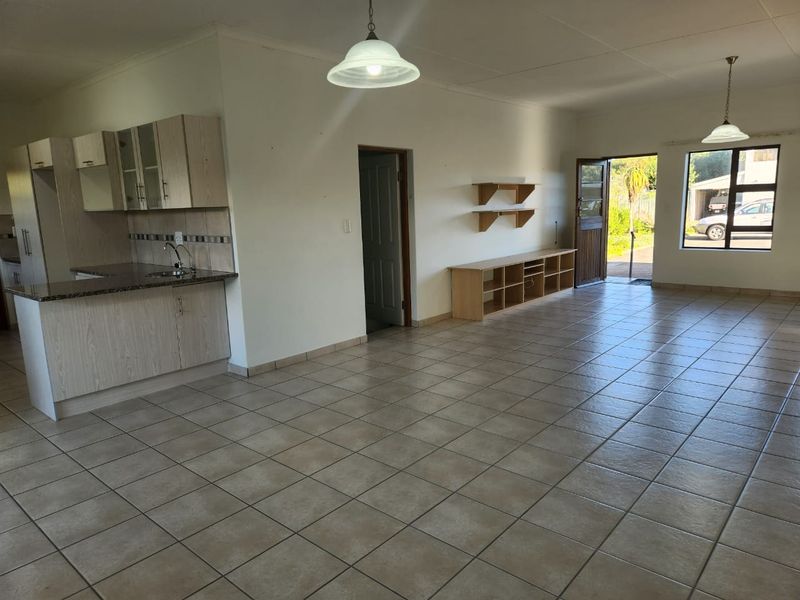 Spacious open-plan living area featuring tiled flooring, a functional kitchen with granite countertops, and direct access to the exterior.