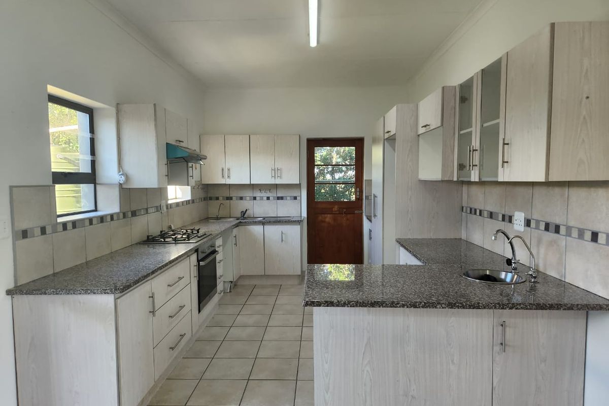 A clean, functional kitchen featuring granite countertops, built-in cabinetry, a gas hob, and tiled flooring with direct access to the exterior.