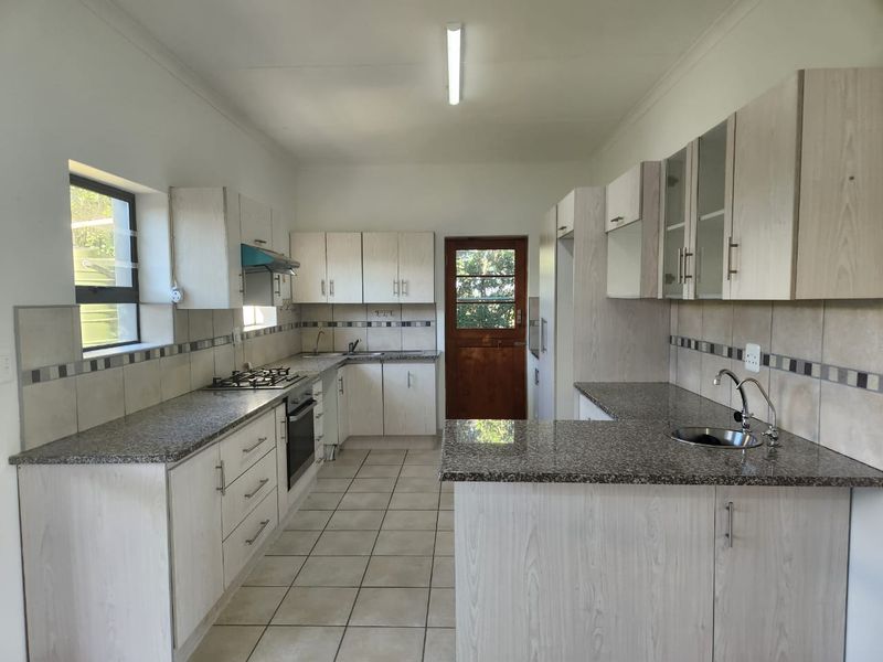 A clean, functional kitchen featuring granite countertops, built-in cabinetry, a gas hob, and tiled flooring with direct access to the exterior.