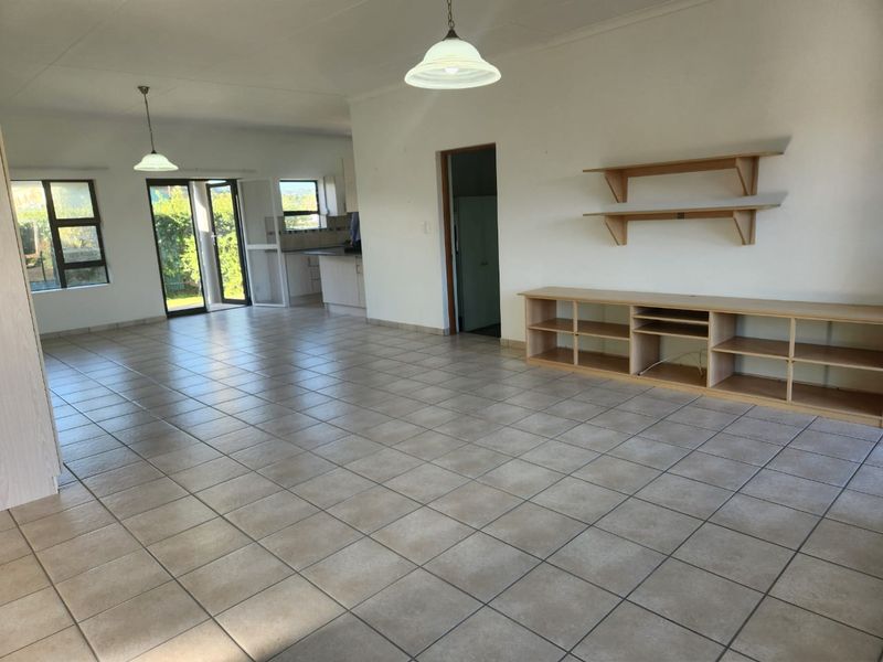 Spacious open-plan living area featuring neutral ceramic floor tiles, built-in shelving, and direct access to the rear garden through sliding doors.