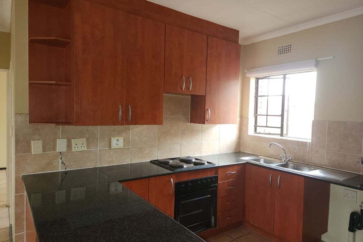 A functional kitchen featuring wood-finish cabinetry, granite countertops, a built-in oven and hob, and a double stainless steel sink with tiled backsplash.