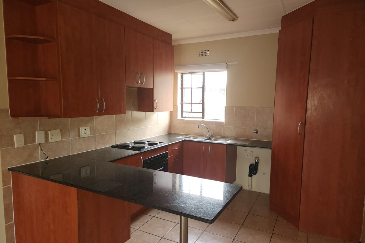 A functional kitchen featuring wood-finish cabinetry, granite countertops, a built-in oven and hob, and tiled flooring, offering a clean and practical workspace.