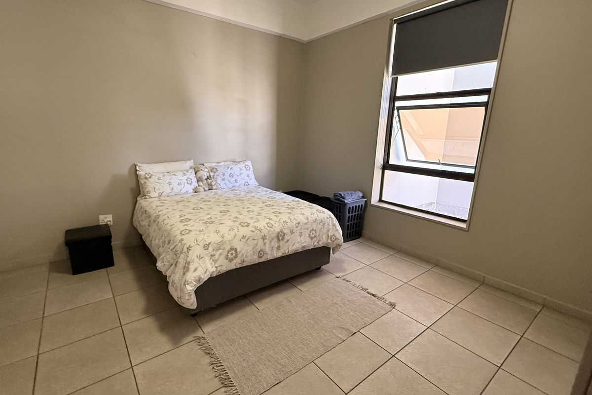 A bedroom featuring neutral wall tones, tiled flooring, and an awning window with a roller blind.