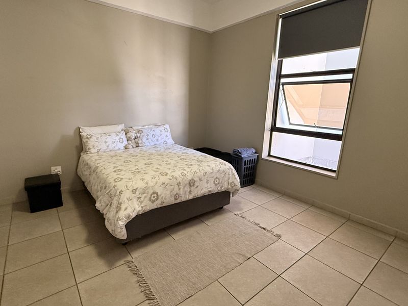 A bedroom featuring neutral wall tones, tiled flooring, and an awning window with a roller blind.