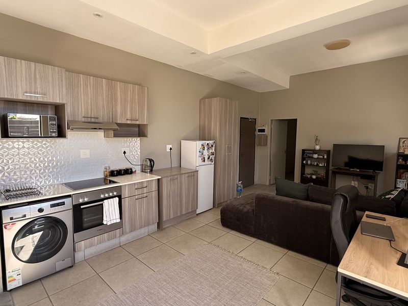Open-plan living area featuring a modern kitchen with wood-finish cabinetry, integrated appliances, tiled flooring, and a combined lounge and workspace layout.