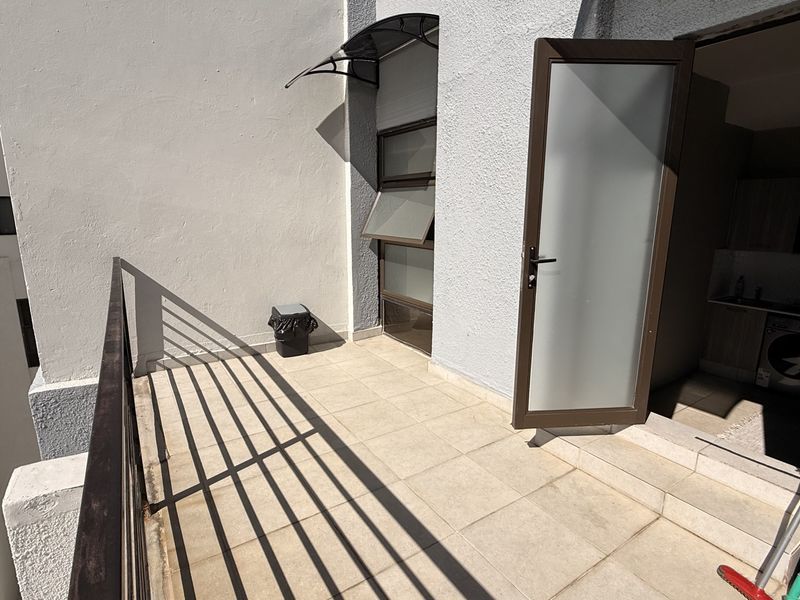 A private balcony featuring tiled flooring, a metal balustrade, and a frosted glass door providing access to the interior living space.