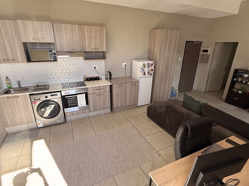 Open-plan living area featuring a modern kitchen with built-in cabinetry, integrated appliances, and tiled flooring throughout.