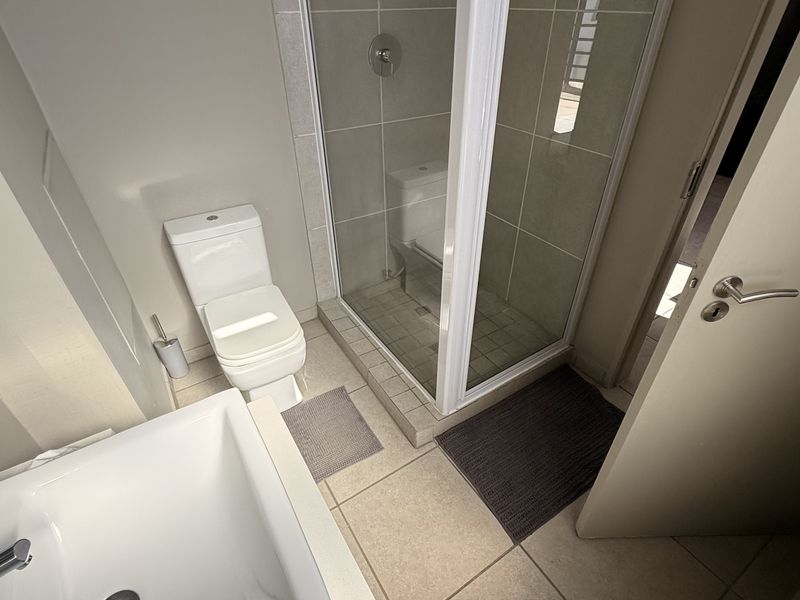 A clean, functional bathroom featuring a separate shower enclosure, bathtub, and toilet with neutral tiled finishes.