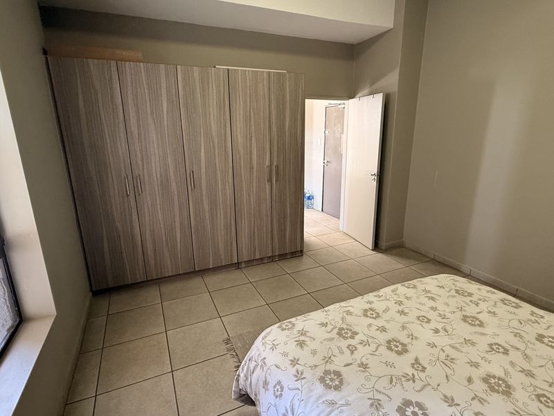 A well-lit bedroom featuring neutral tiled flooring, ample built-in cupboard storage, and a large window providing natural light.