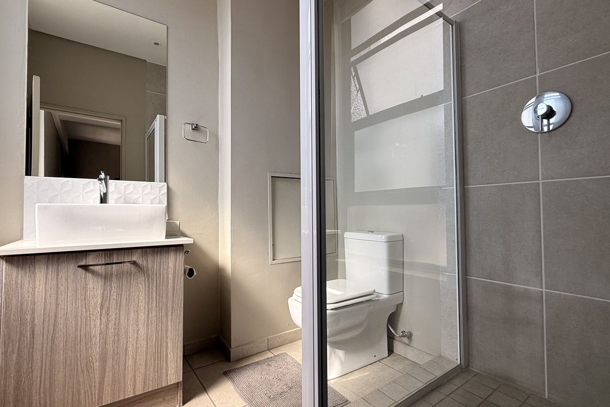 Modern bathroom featuring a wood-finish vanity with a vessel sink, a glass-enclosed shower, and neutral wall and floor tiling.