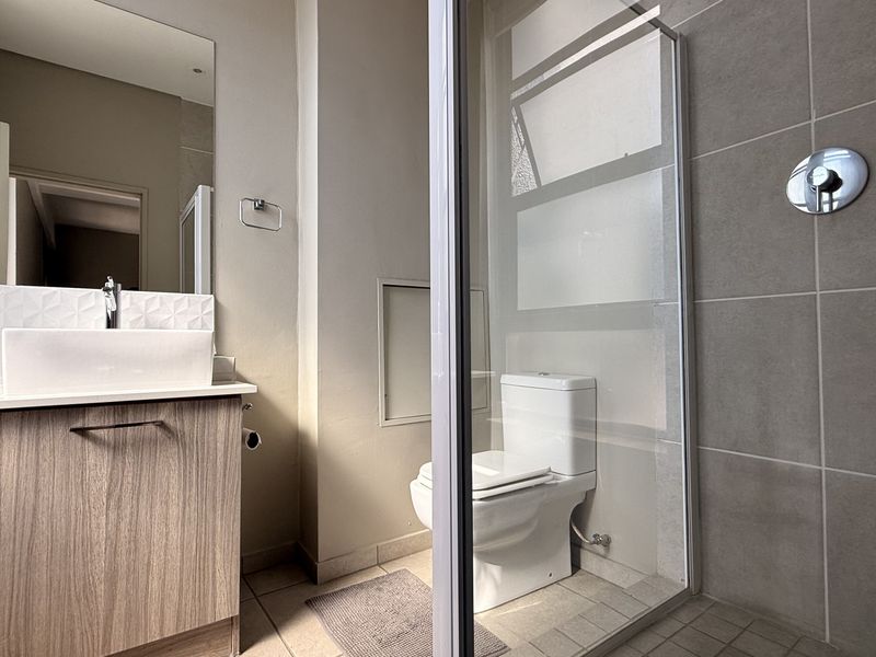 Modern bathroom featuring a wood-finish vanity with a vessel sink, a glass-enclosed shower, and neutral wall and floor tiling.