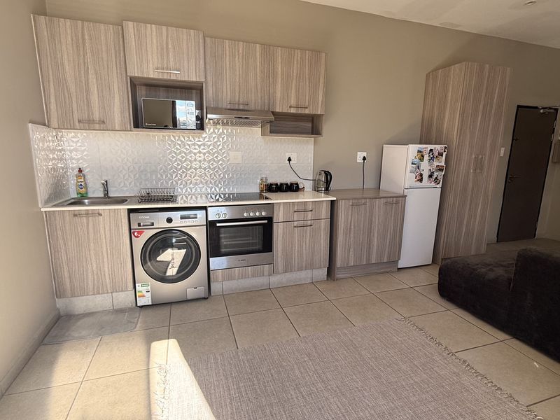 Open-plan kitchen featuring modern wood-look cabinetry, stainless steel oven, extractor fan, and tiled backsplash, seamlessly integrated into the living area.