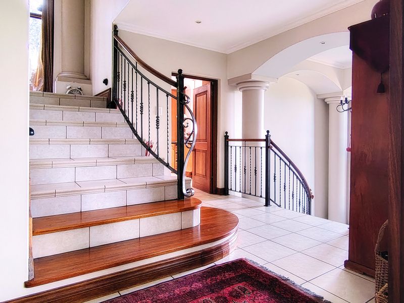 Grand entrance hall featuring a tiled staircase with wooden treads, wrought iron balustrades, and elegant architectural columns leading to an arched hallway.