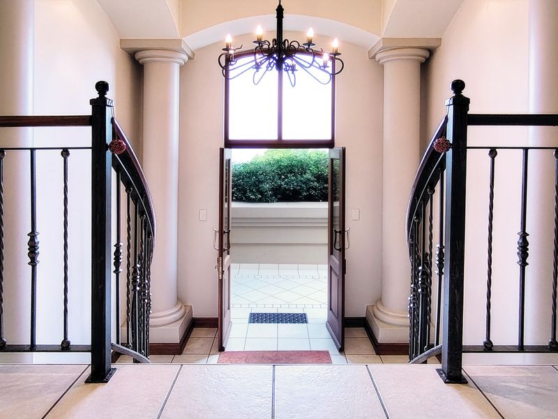Grand entrance foyer featuring elegant classical columns, a wrought iron staircase balustrade, and a central chandelier leading to an outdoor patio area.