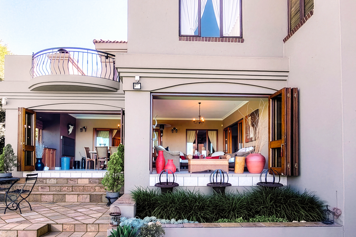 Rear elevation featuring a stone-paved patio, large folding doors opening to the living area, and an upper-level balcony with wrought iron railings.