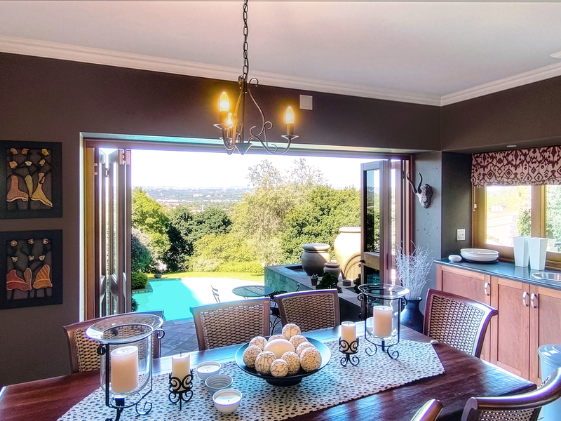 Open plan dining area featuring bi-fold doors opening to a pool deck with scenic views, complemented by built-in cabinetry and a fireplace.