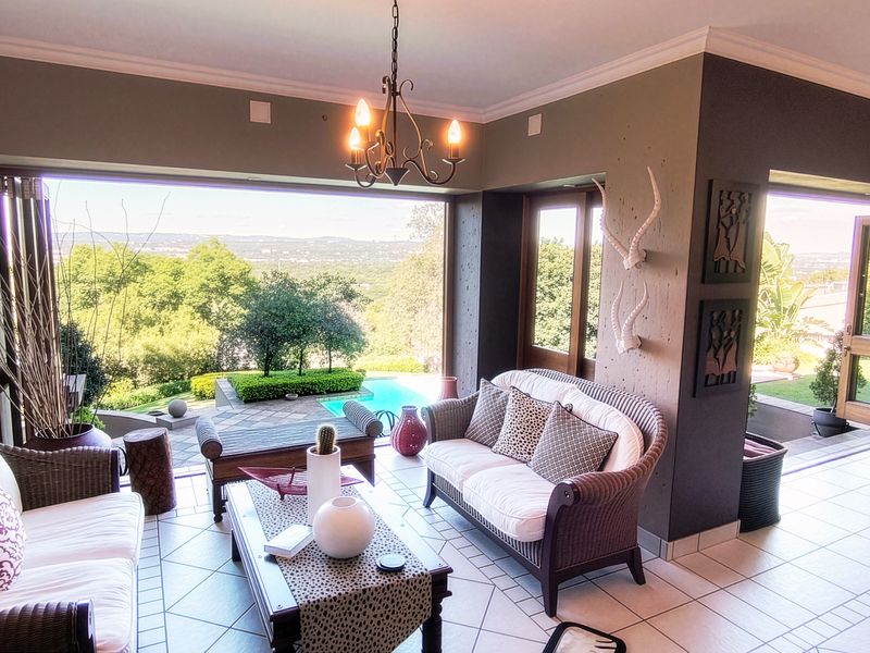 Spacious open-plan living area featuring tiled floors, elegant chandelier lighting, and large folding glass doors that open to a scenic outdoor pool view.