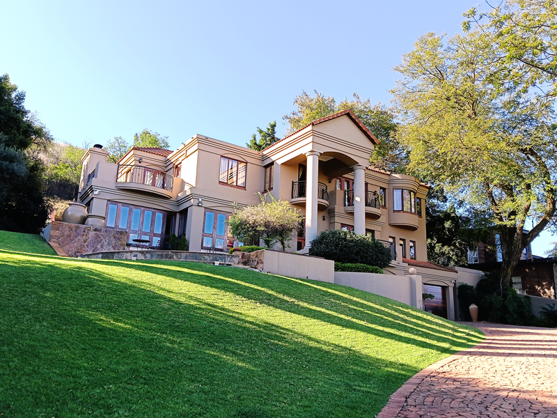 A grand multi-story residence featuring stone accents, multiple balconies, columns, and a well-maintained lawn with a paved driveway.
