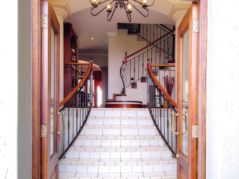 Grand entrance featuring a tiled staircase with ornate wrought iron railings, wooden double doors, and a decorative chandelier.