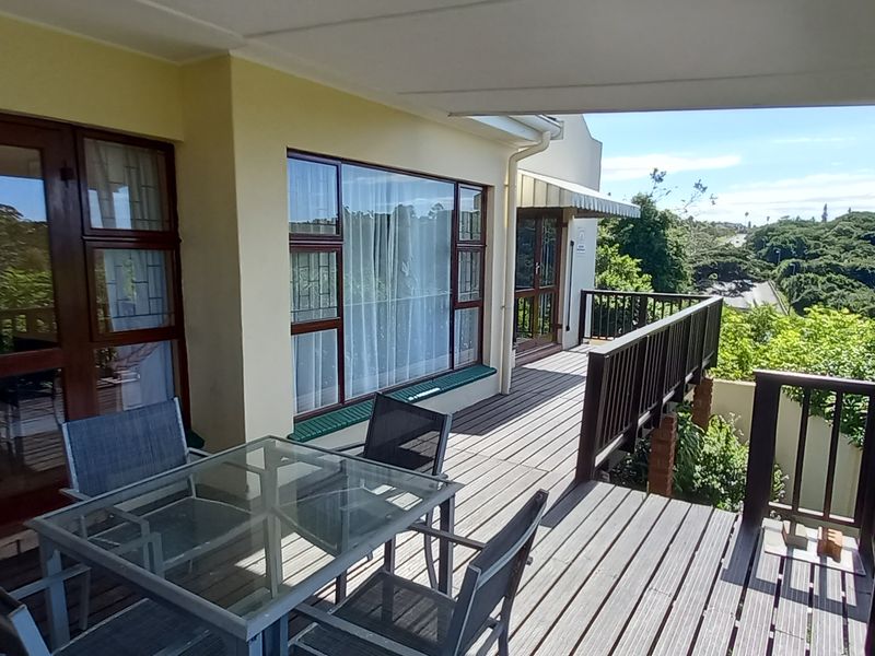 Spacious elevated timber deck balcony featuring a covered roof, timber balustrades, and direct access to the interior living area through sliding glass doors.