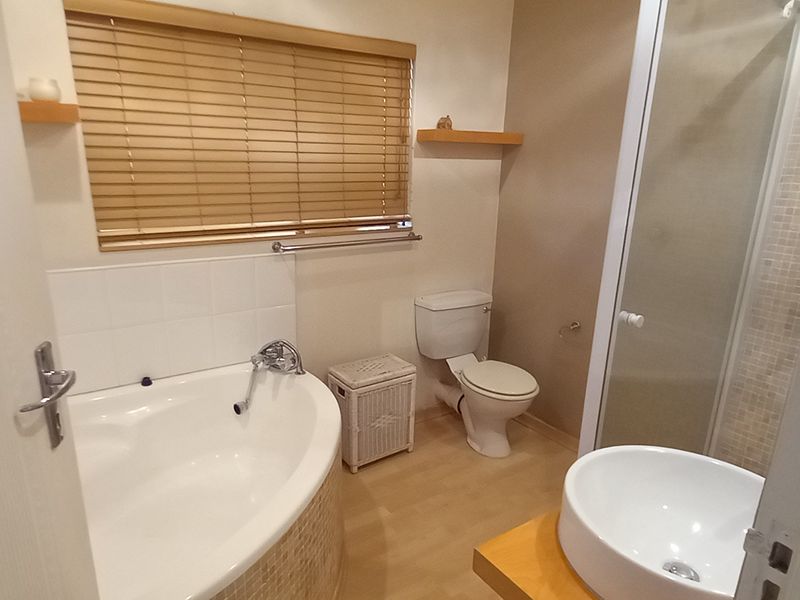 A well-appointed bathroom featuring a corner bathtub, separate shower enclosure, vessel sink on a wooden vanity, and neutral finishes.