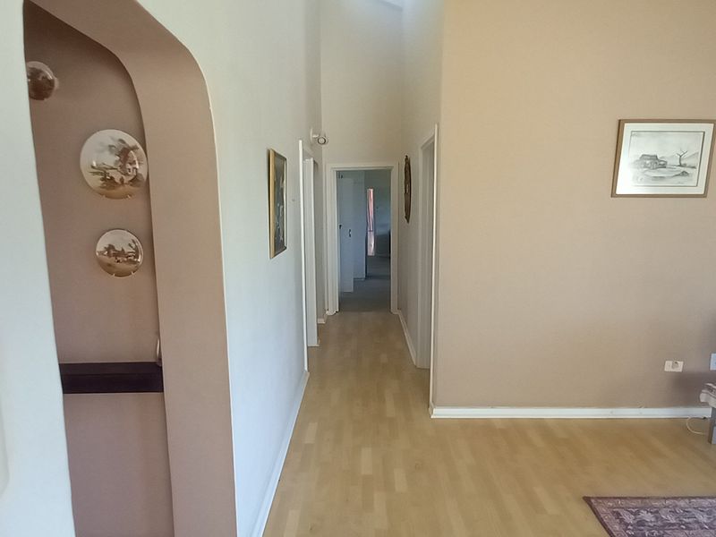 A living area featuring laminate flooring, an arched entryway, and an integrated intercom system, leading into a central hallway.