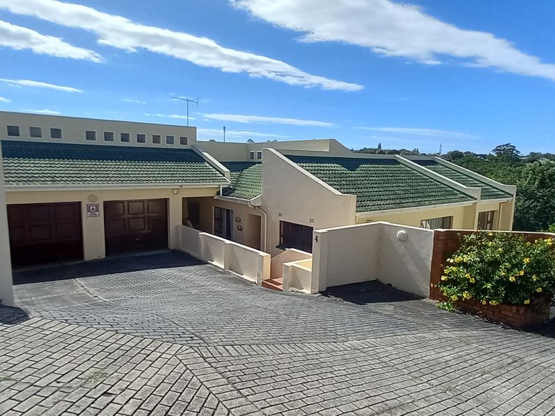 Front elevation of a townhouse featuring a double garage, paved driveway, and tiled roof, situated in a residential complex.