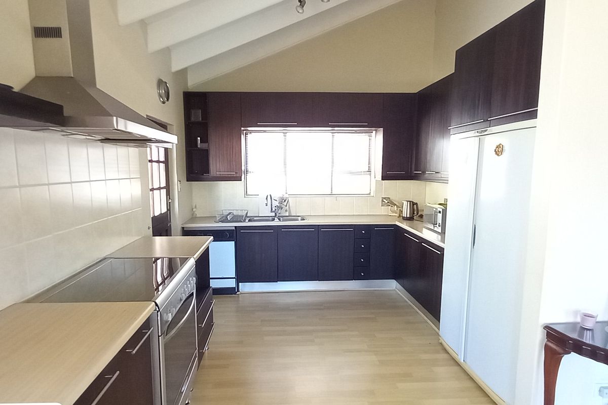 A functional kitchen featuring dark wood cabinetry, laminate countertops, a built-in oven with hob, and a vaulted ceiling providing a spacious feel.